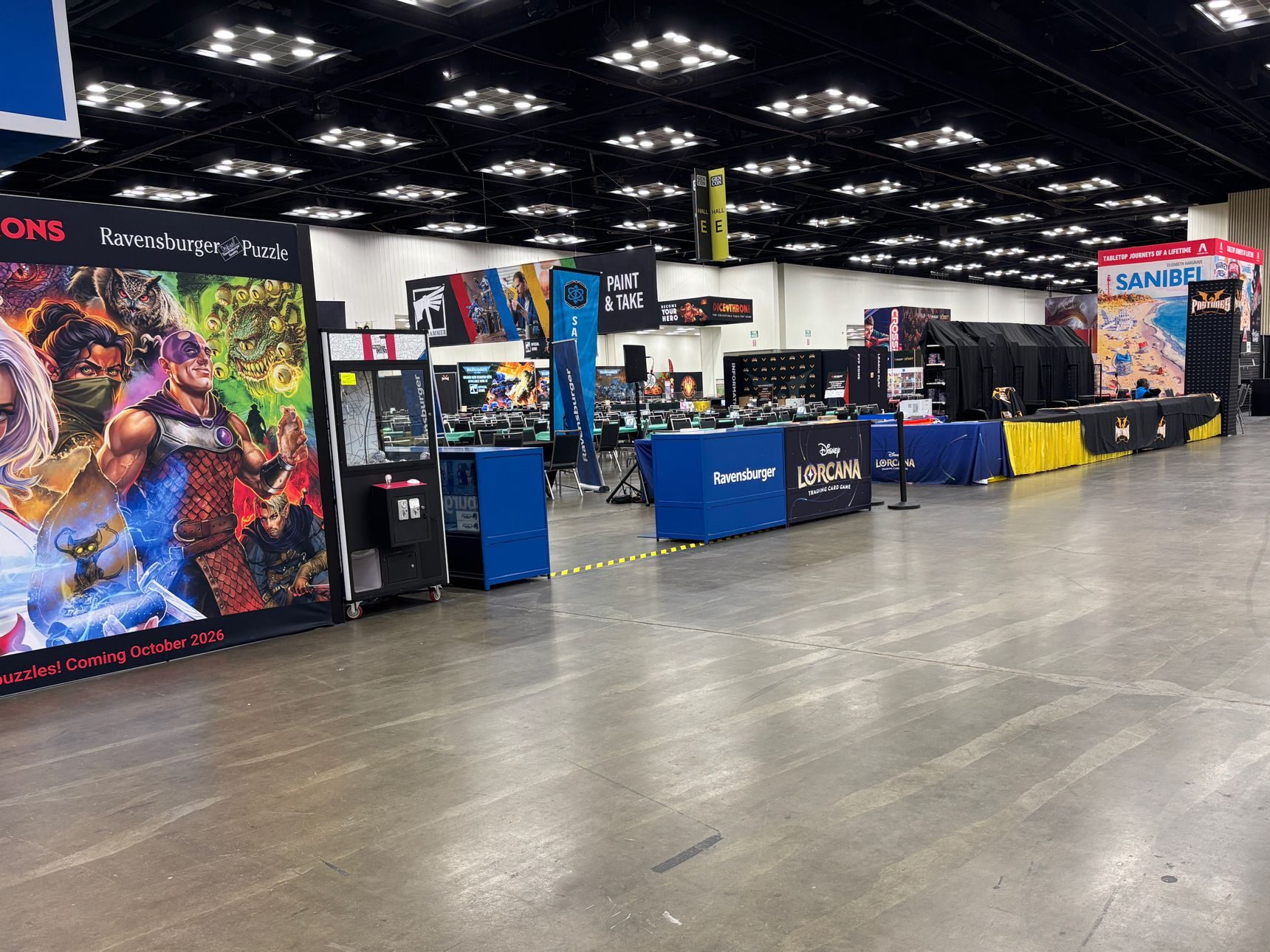 Empty convention center show floor with board game exhibitor booths including Ravensburger, Disney Lorcana, and Warhammer, set up before doors open